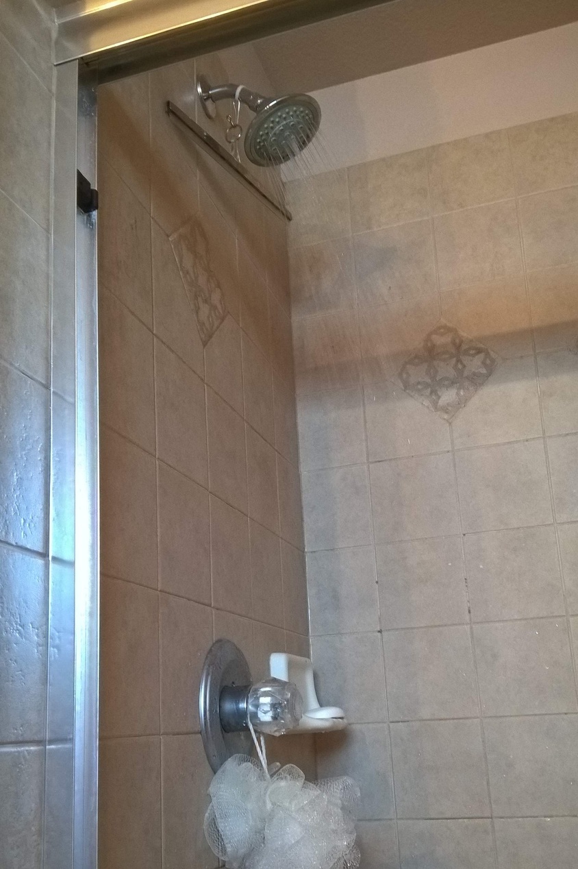 Een standaard binnendouche met beige tegels en een glazen deur, waar het water stroomt.